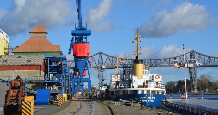 Foto des Kreishafens Rendsburg. Es liegt ein Schiff am Kai im Hintergrund ist die Rendsburger Hochbrücke zu sehen.